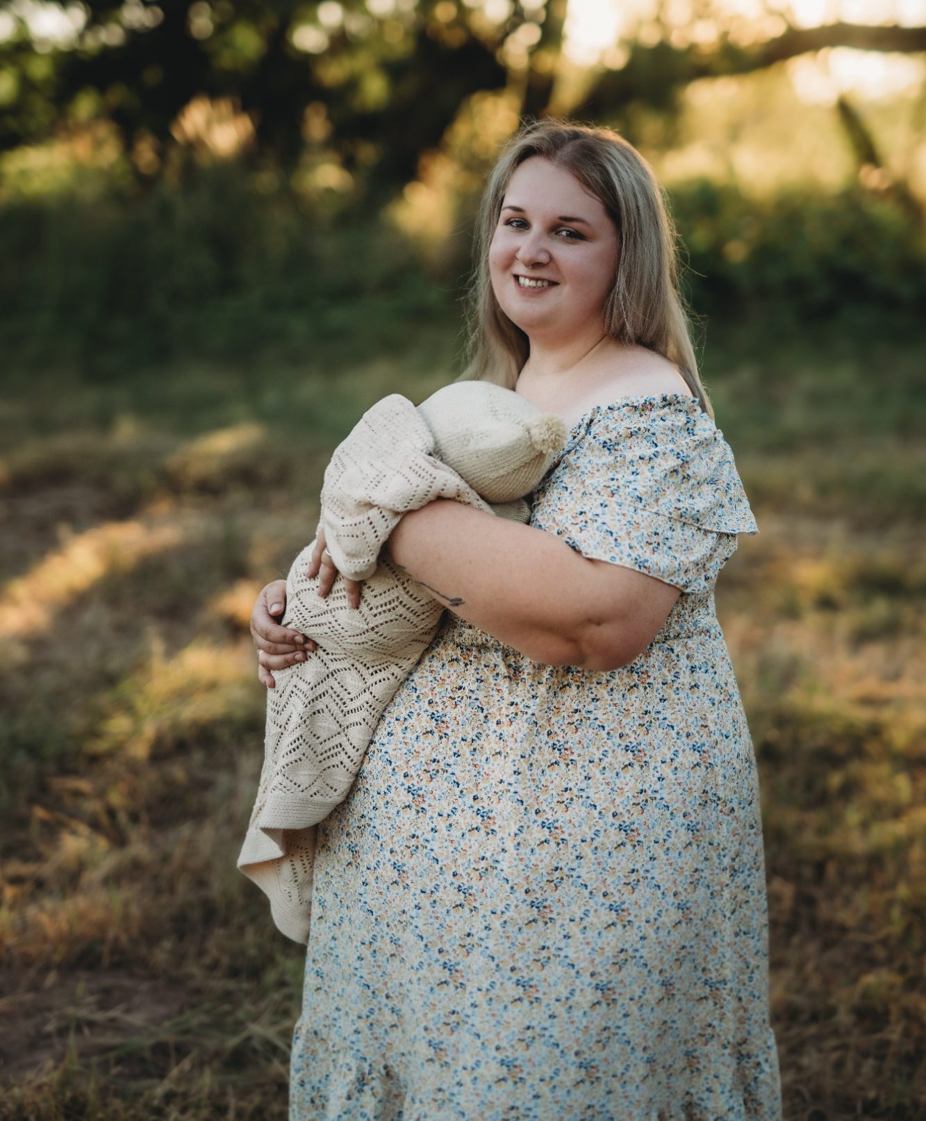 Lächelnde Frau mit einem Baby in einem ländlichen Umfeld, umgeben von Natur.